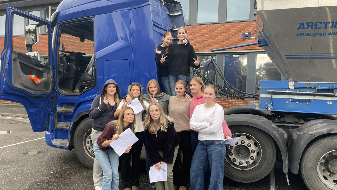 Mange jenter fra ungdomsskoletrinnet står foran en semitrailer. 
