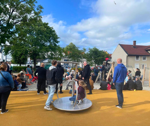 Barn og foreldre leker på lekeplass. en liten karusell i forgrunn.