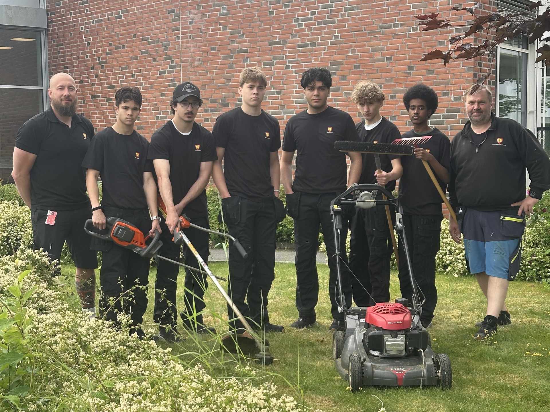 Fra venstre teamansvarlig Pål Mangseth med sommervikarene Eric (16), Mohamed (16), Lucas (17), Adam (17) , Abas (17)  og Vilmos (15), som alle skal ha sommerjobb i bygningsdrift i Fredrikstad kommune. Til høyre servicesnekker Morten Ek. Før oppstart fikk de opplæring i sikker bruk av småmaskiner.