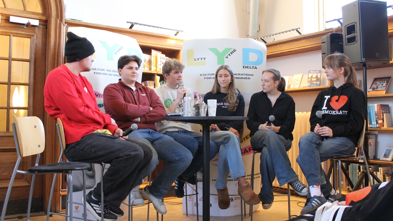 Ungdommer sitter på barstoler i en panelsamtale. 