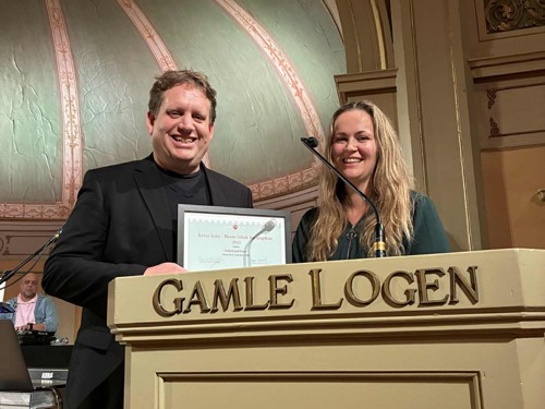 To personer står på et podium og viser fram en pris. 