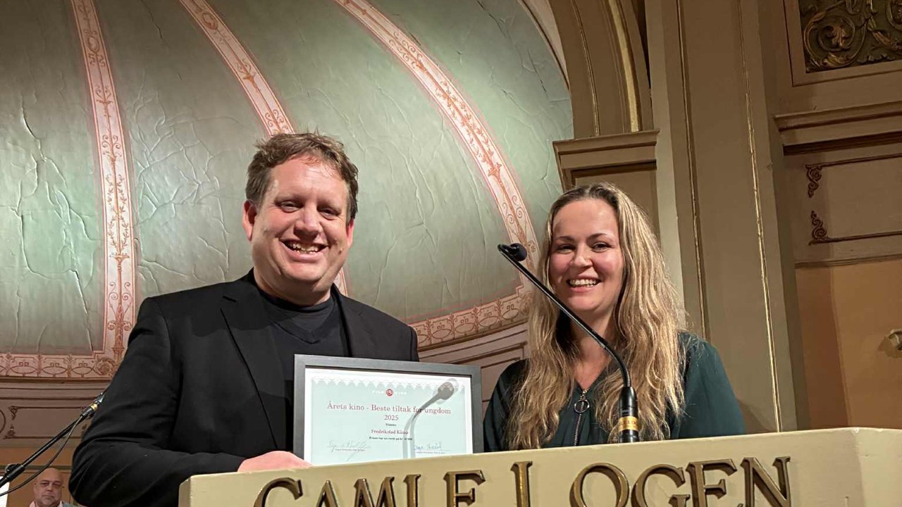 To personer står på et podium og viser fram en pris. 