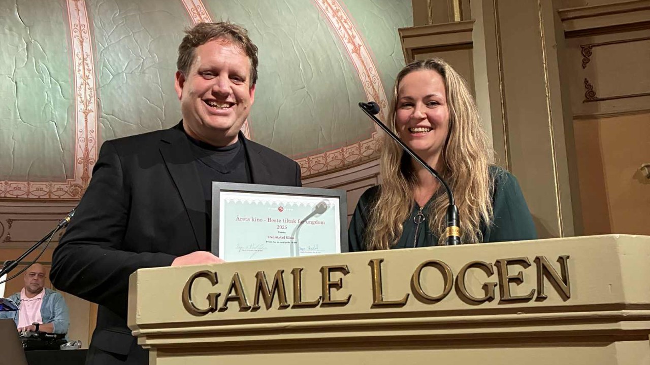 To personer står på et podium og viser fram en pris. 