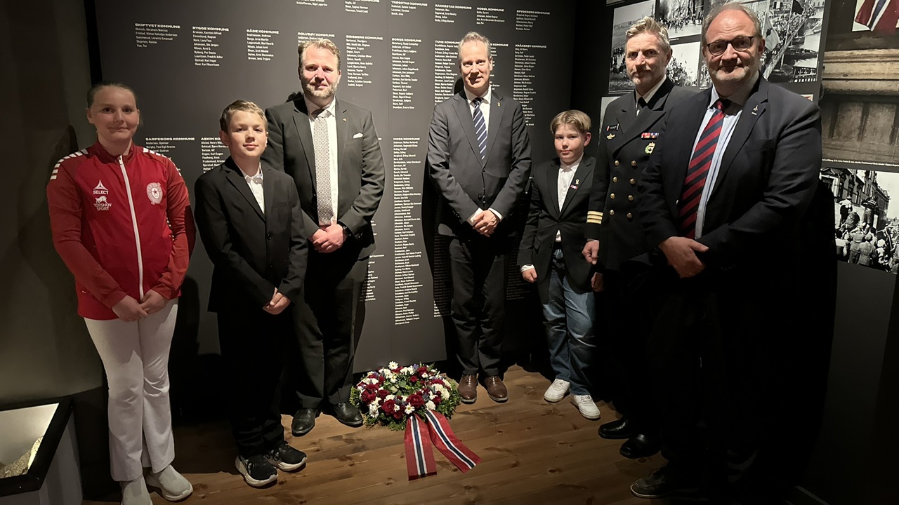 Tre barn fikk æren av å legge ned krans ved minneveggen over krigens falne fra Østfold på Fredrikstad museum. Veggen bærer 569 navn og er det eneste stedet i fylket hvor alle navnene er samlet. Fra venstre: Signe, Nils August, undertegnede, statsråd Jon-Ivar Nygård, Mathias, Jarle Tranøy (stabssjef og nestkommanderende ved Oslofjord Heimevernsdistrikt 01), og statsstipendiat Petter Ringen Johannessen.