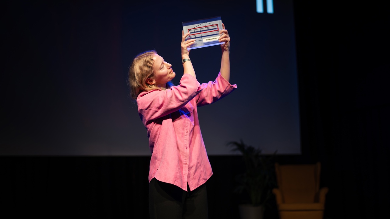 Ung kvinne i rosa skjorte holder opp en pris på en scene