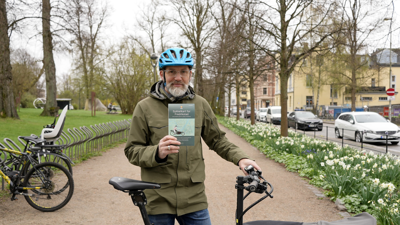 En mann står bak en sykkel og holder opp et kart