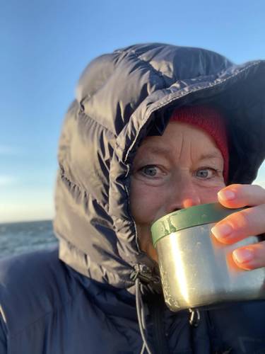 Dame med hette drikker kaffe fra termos.