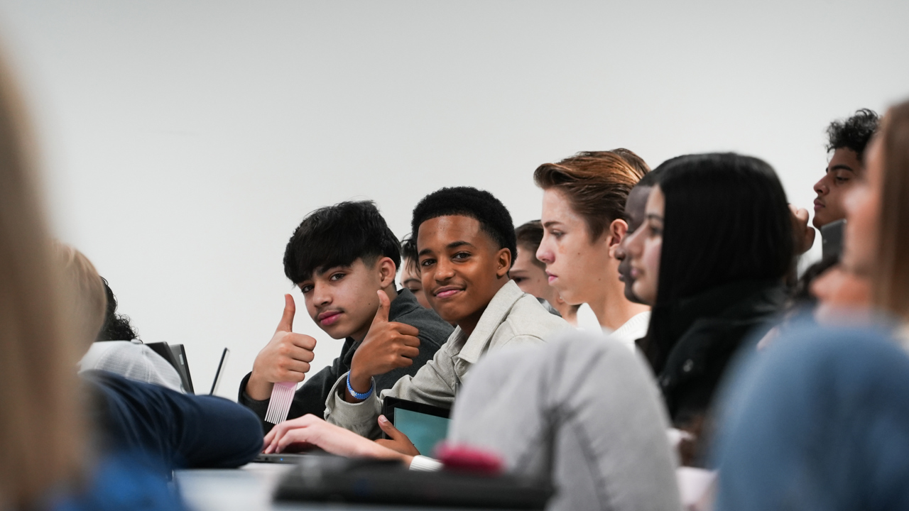 Elever følger med på undervisning og titter i kamera og smiler 