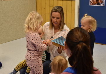 en voksen dame sitter på gulvet sammen med barn og leker. 
