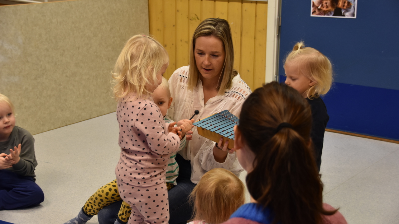 en voksen dame sitter på gulvet sammen med barn og leker. 