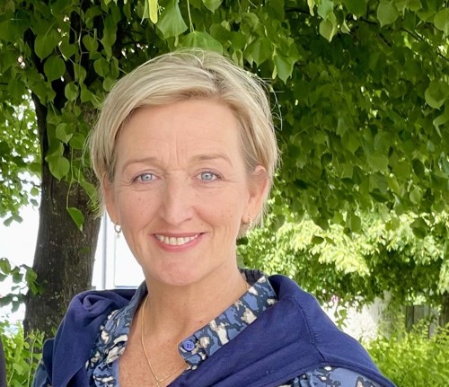 Kvinne smiler med grønne trær bak