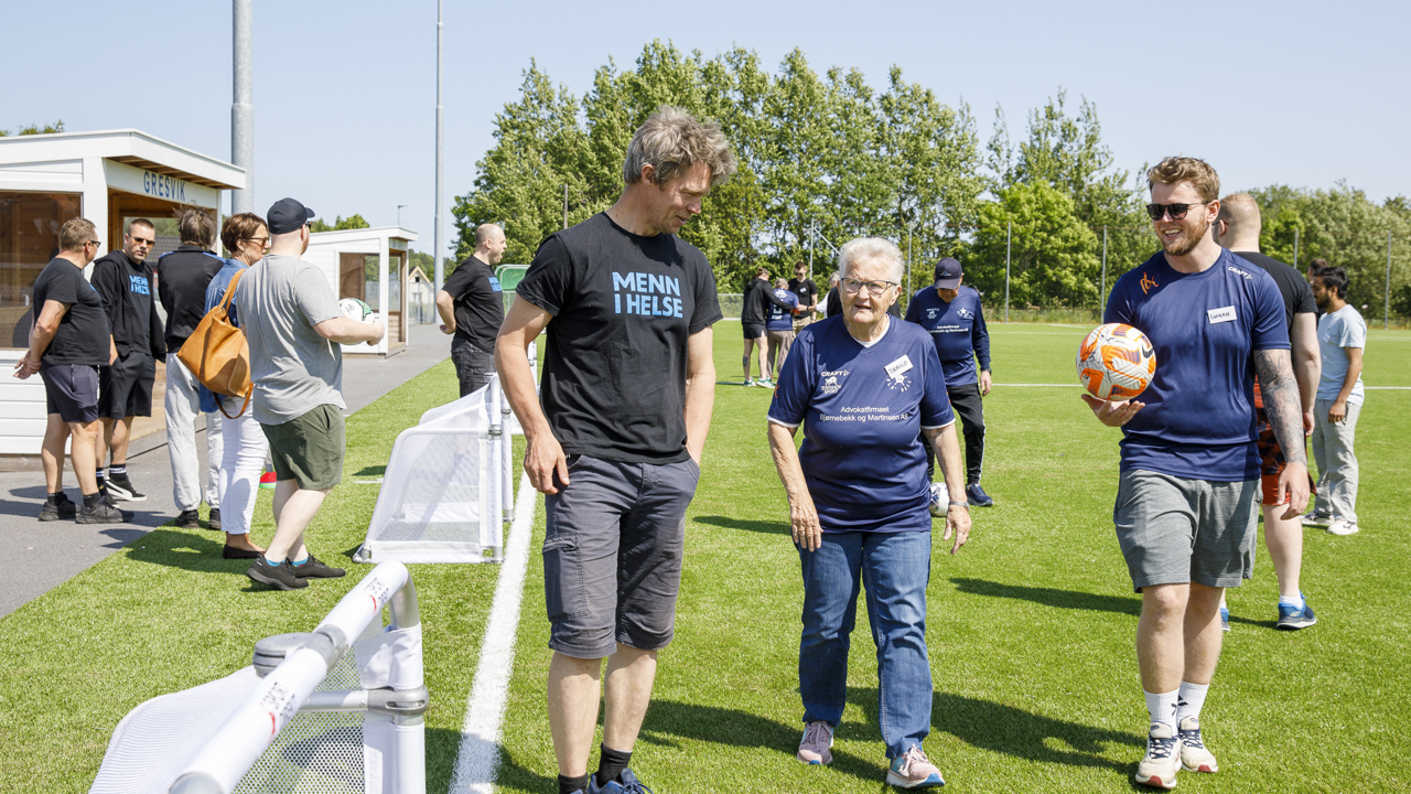 To menn og en dame går på en fotballbane. 